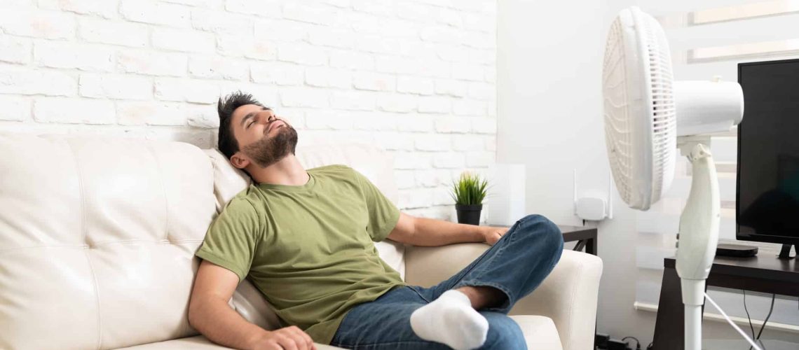 Hispanic mid adult man relaxing on sofa in front of fan in living room at home